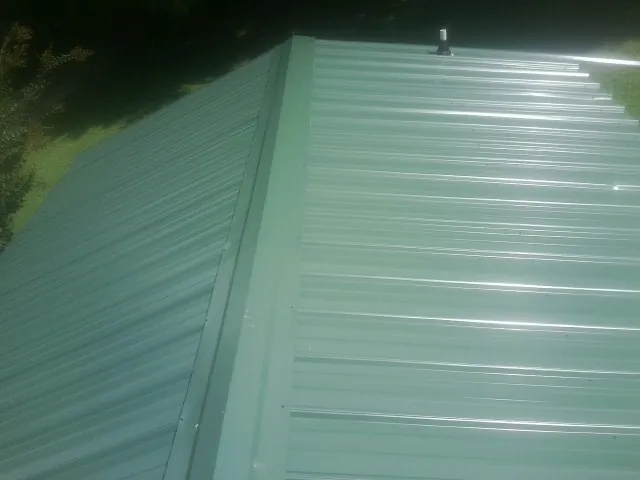 New green metal panels meeting at the ridge of a roof — Flat Roof Repair work by our crew in Caldwell